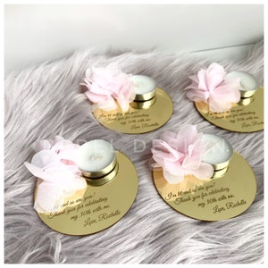 May include: Four gold round mirrored candle holders with a pink flower on top and a small white tea light candle. The holders have a personalized message engraved on them that says "I'm lit and so are you! Thank you for celebrating my 30th with me. Love, Rochelle"