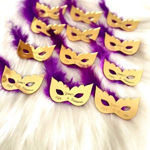 Puede incluir: Favores de fiesta en forma de m&aacute;scara de mascarada de color dorado con plumas moradas. Cada m&aacute;scara tiene el texto "Jeane's Fippy & Fabulous" escrito en ella.