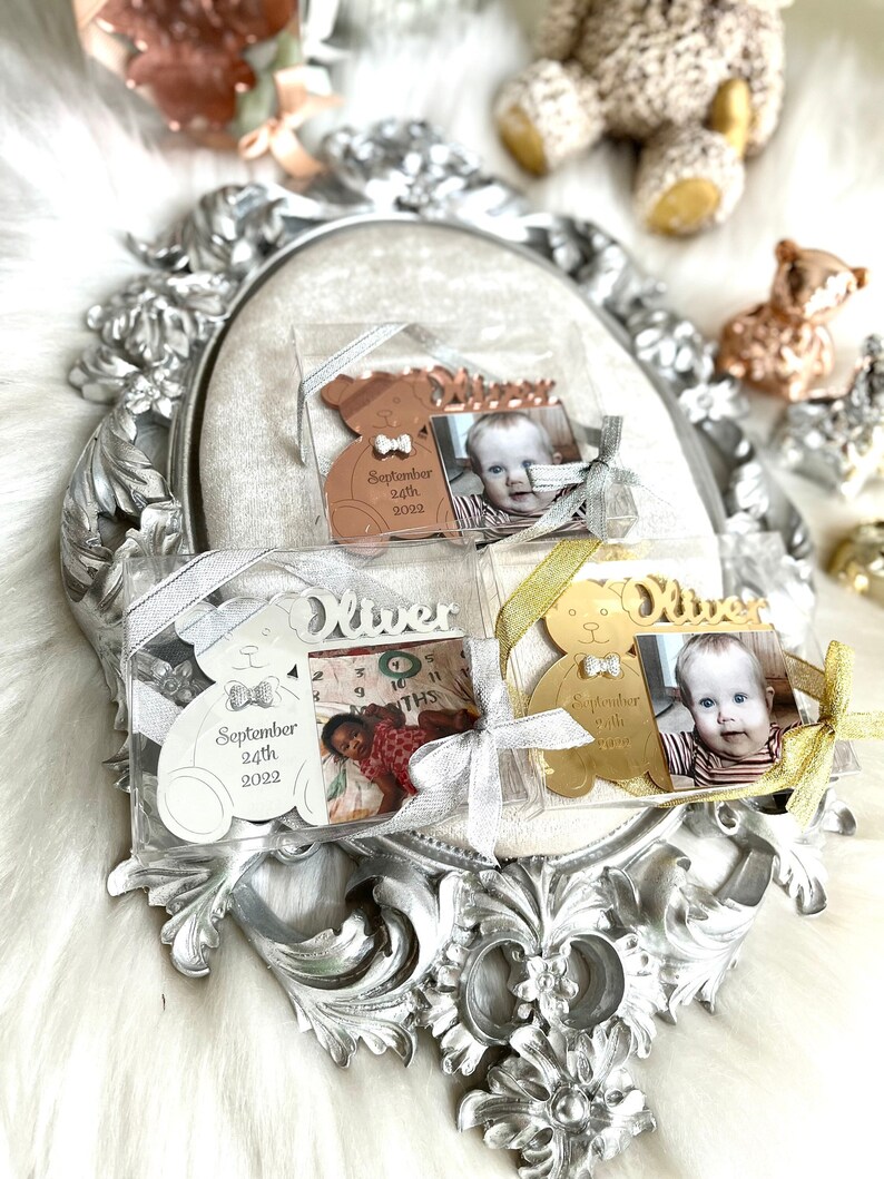 May include: Three silver, gold, and copper teddy bear ornaments with a photo frame and the name "Oliver" engraved on them. The ornaments also include the date "September 24th, 2022".