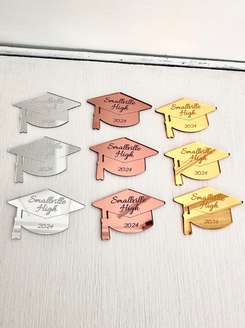May include: Nine graduation cap-shaped acrylic ornaments in three different colors: silver, rose gold, and gold. Each ornament features the text "Smallville High 2024".