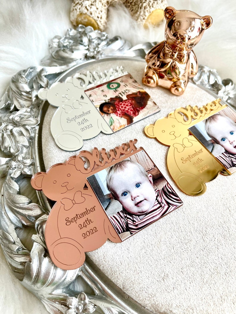 May include: Three personalized mirrored acrylic bear ornaments with a photo frame. The ornaments are in silver, gold, and rose gold. Each ornament has the name "Oliver" and the date "September 24th, 2022".