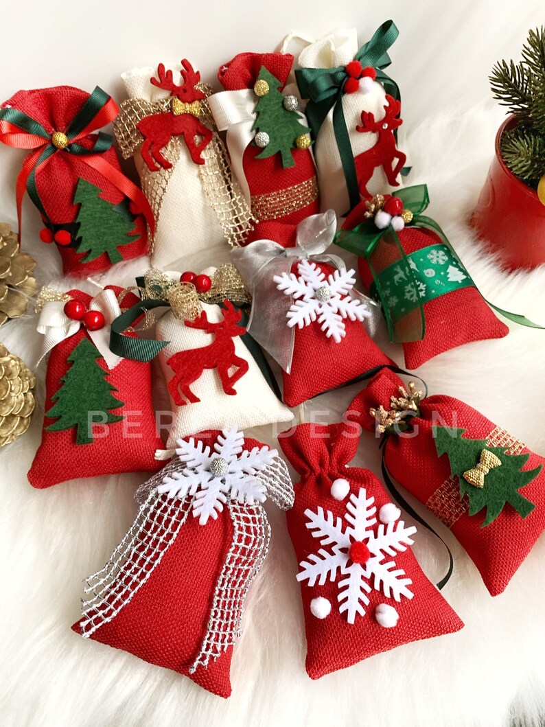 Puede incluir: Surtido de peque&ntilde;as bolsas de regalo de tela roja y blanca con diversas decoraciones de tem&aacute;tica navide&ntilde;a, incluyendo copos de nieve, renos y &aacute;rboles de Navidad. Las bolsas est&aacute;n llenas de una sustancia blanca y atadas con una cinta.