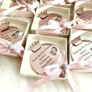 May include: Pink and white favor boxes with a rose gold crown and a round mirror with the text "Thank You For Making Gianna's 1st Birthday Very Special!"