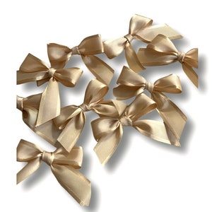 May include: A set of ten gold satin bows. The bows are arranged in a cluster, with some overlapping. The bows are all the same size and shape, and they have a soft, luxurious feel.