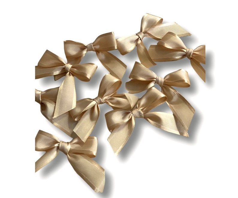 May include: A set of ten gold satin bows. The bows are arranged in a cluster, with some overlapping. The bows are all the same size and shape, and they have a soft, luxurious feel.