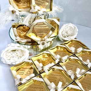 May include: Gold favor boxes with a round mirror inside. Each mirror has a personalized message with a teddy bear graphic and the text "Thank you for making Olivia's first birthday very special".