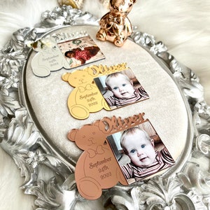 May include: Three mirrored photo frames shaped like teddy bears with a photo of a baby and the name "Oliver" and the date "September 24th, 2022" engraved on each frame. The frames are silver, gold, and rose gold.