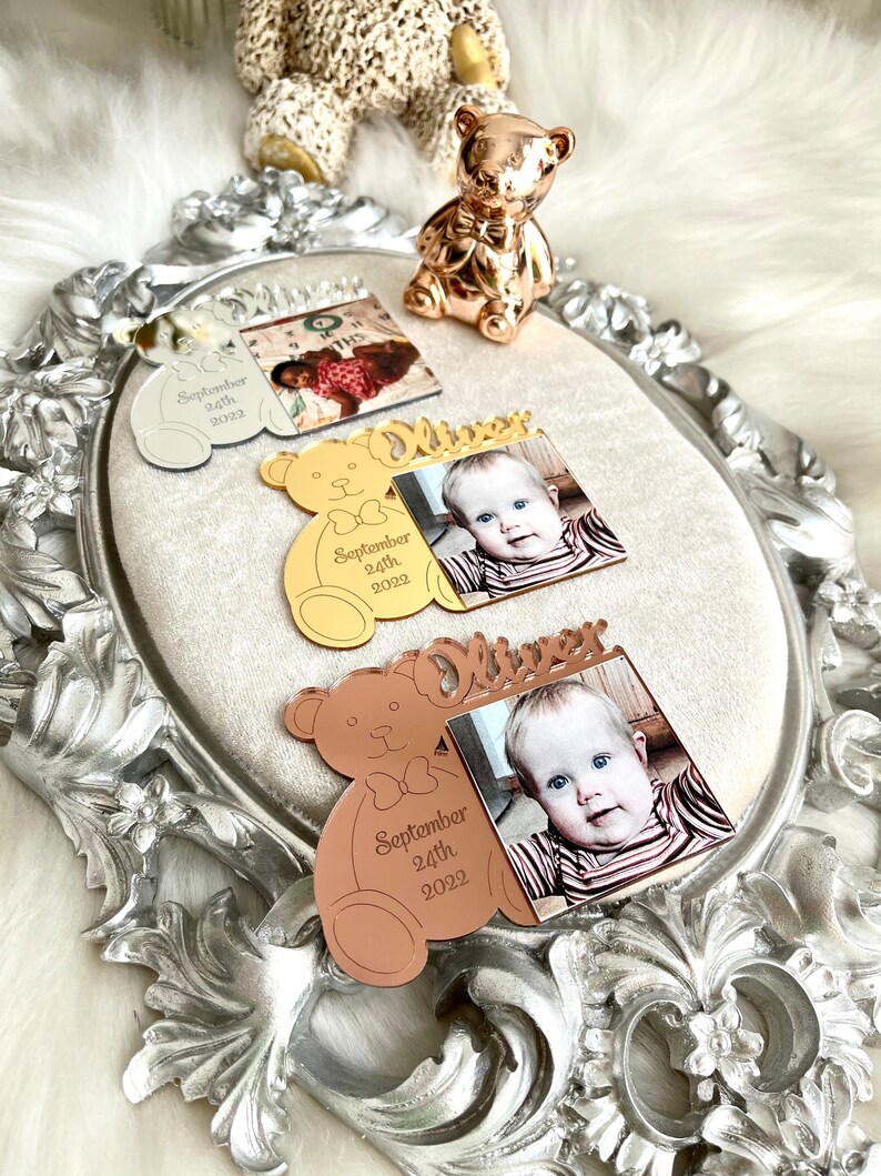 May include: Three mirrored photo frames shaped like teddy bears with a photo of a baby and the name "Oliver" and the date "September 24th, 2022" engraved on each frame. The frames are silver, gold, and rose gold.