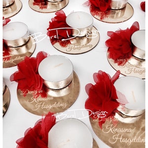 May include: Gold mirrored candle holders with red tulle flowers and white tea lights. Each holder has the text "Deniz in Kinasina Hosgeldiniz" engraved on it.