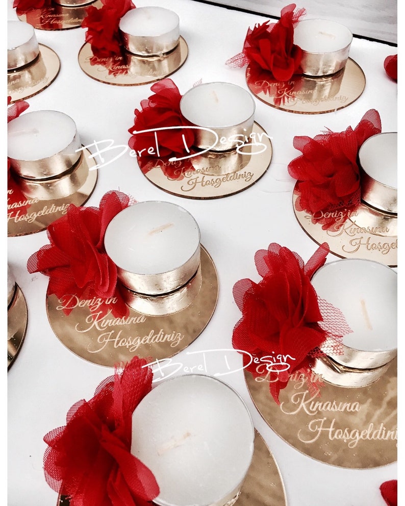 May include: Gold mirrored candle holders with red tulle flowers and white tea lights. Each holder has the text "Deniz in Kinasina Hosgeldiniz" engraved on it.