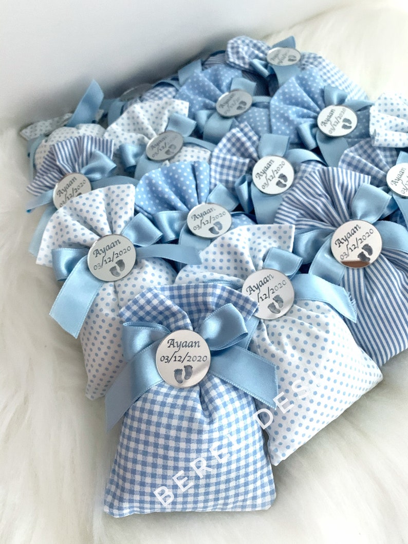 May include: Blue and white gingham favour bags with a silver circle tag that says "Ayaan 03/12/2020" and a small footprint design.