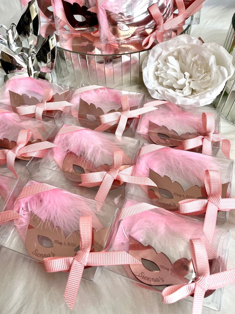 May include: Pink and gold party favours with a mask design and the name "Sienna's" and the date "May 6, 2023".