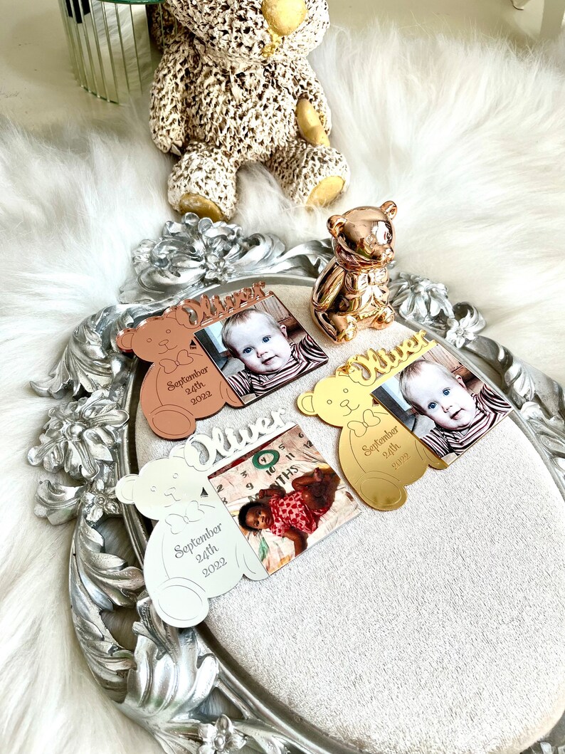May include: Three silver, gold, and rose gold bear-shaped photo frames with the name "Oliver" engraved on them. Each frame has a photo of a baby and the date "September 24th, 2022".