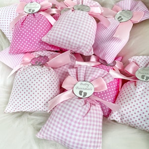 May include: Pink and white fabric gift bags with a silver tag that says "Baby Bassalali" and a footprint design. The bags are tied with pink ribbon.