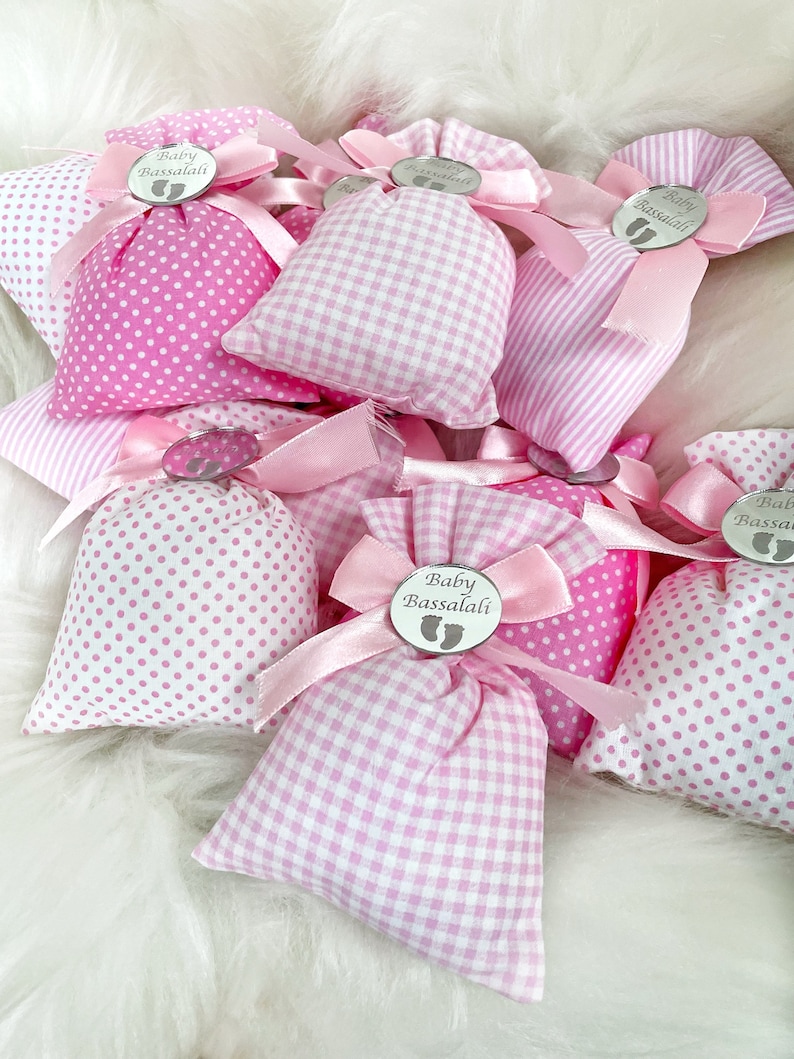 May include: Pink and white fabric gift bags with a silver tag that says "Baby Bassalali" and a footprint design. The bags are tied with pink ribbon.