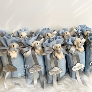 Puede incluir: Bolsas de regalo azul claro con un peque&ntilde;o osito de peluche que lleva una pajarita. Cada bolsa tiene una etiqueta de nube plateada con el texto "Baby CJ" en ella.