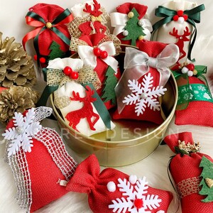 Puede incluir: Una colecci&oacute;n de peque&ntilde;as bolsas de arpillera roja y blanca con diversas decoraciones navide&ntilde;as, incluyendo copos de nieve, renos y &aacute;rboles de Navidad. Las bolsas est&aacute;n dispuestas en un recipiente de metal dorado.