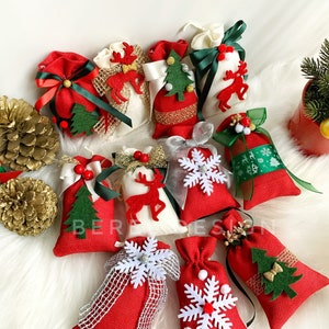 Puede incluir: Surtido de peque&ntilde;as bolsas de regalo de Navidad rojas y blancas con varios dise&ntilde;os festivos, incluyendo renos, copos de nieve y &aacute;rboles de Navidad. Las bolsas est&aacute;n decoradas con cintas y lazos.