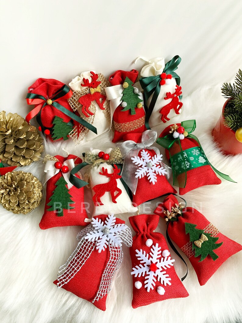 Puede incluir: Surtido de peque&ntilde;as bolsas de regalo de Navidad rojas y blancas con varios dise&ntilde;os festivos, incluyendo renos, copos de nieve y &aacute;rboles de Navidad. Las bolsas est&aacute;n decoradas con cintas y lazos.
