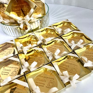May include: Gold favor boxes with a round, gold mirror inside. The mirror has a personalized message that says "Thank you for making Olivia's first birthday very special March 30, 2020".