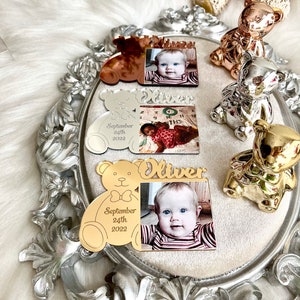 May include: Gold, silver, and rose gold teddy bear photo frames with a baby's photo and the name "Oliver" and the date "September 24th, 2022".