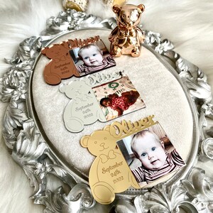 May include: Three gold, silver, and rose gold bear-shaped photo frames with a photo of a baby boy and the text "Oliver September 24th 2022".