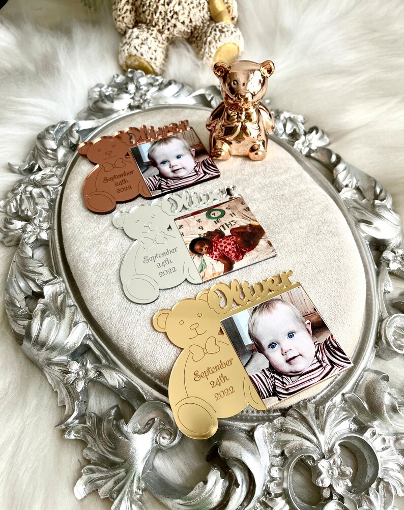 May include: Three gold, silver, and rose gold bear-shaped photo frames with a photo of a baby boy and the text "Oliver September 24th 2022".