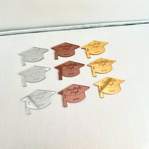 May include: Eight graduation cap shaped mirror acrylic ornaments in gold, silver, and rose gold. Each cap has the text "Smallville High 2024" engraved on it.