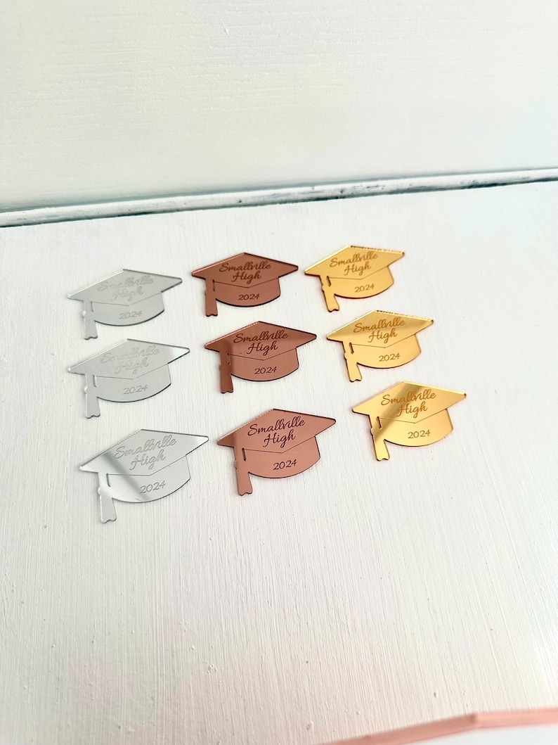 May include: Eight graduation cap shaped mirror acrylic ornaments in gold, silver, and rose gold. Each cap has the text "Smallville High 2024" engraved on it.