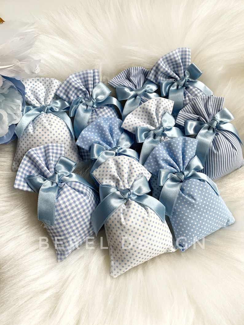 May include: A group of small blue and white fabric bags with blue ribbon ties. The bags are decorated with gingham and polka dot patterns.