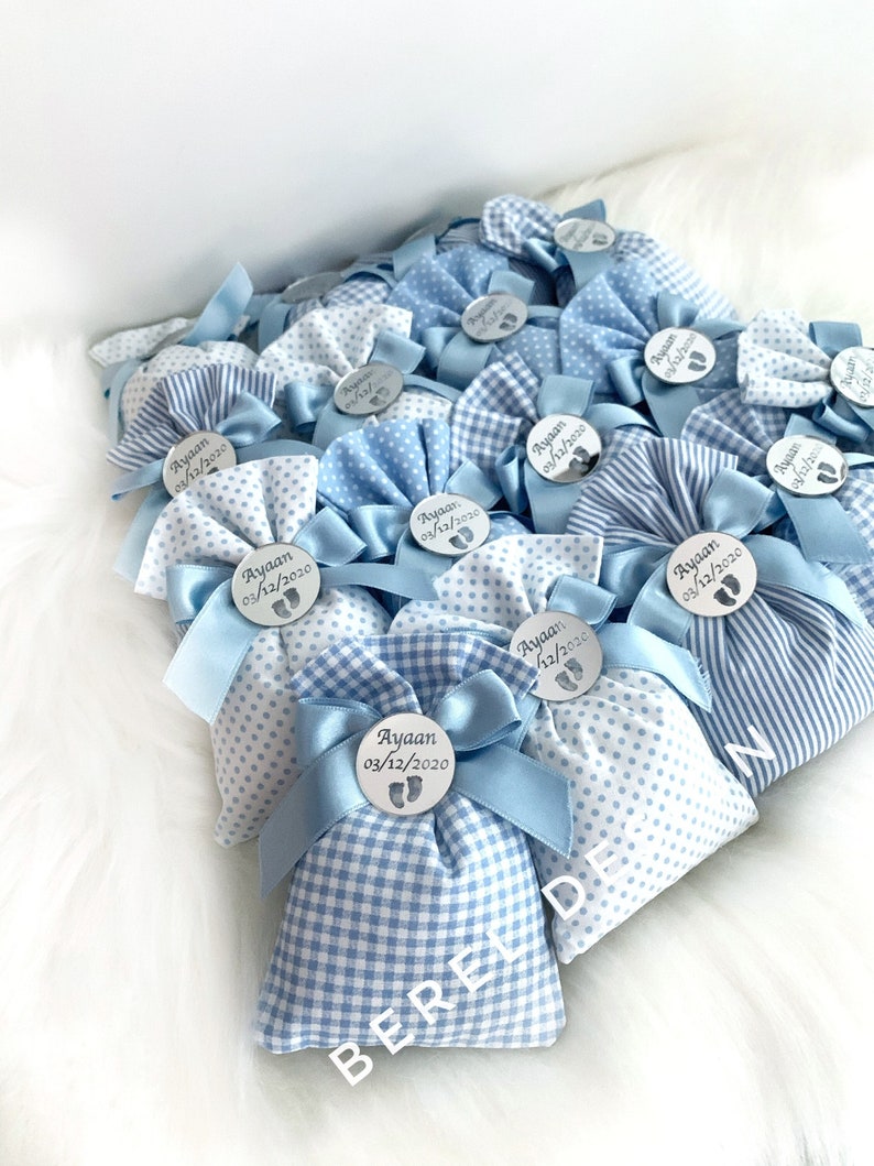 May include: Blue and white gingham fabric favour bags with a blue ribbon and a silver circle tag with the name "Ayaan" and a date.