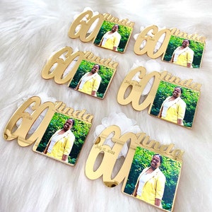 May include: Gold-colored acrylic mirror plaques with the number 60 and the name Linda. Each plaque has a small square photo of a person in a yellow shirt. The date July 15, 2022 is printed on the plaques.