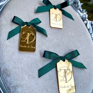 May include: Three gold mirror tags with green ribbon bows. Each tag has the letters "T" and "D" in a cursive font, with the text "Tiandra & Tyray" below.