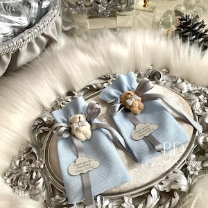 Puede incluir: Dos bolsas de regalo azul claro con cinta gris y un peque&ntilde;o amuleto de oso de peluche. Cada bolsa tiene una etiqueta plateada con el texto "&iexcl;Gracias por duchar a Baby Vinny!"