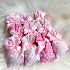 May include: A group of pink fabric gift bags with white polka dots and gingham patterns. The bags are tied with pink satin ribbon bows.
