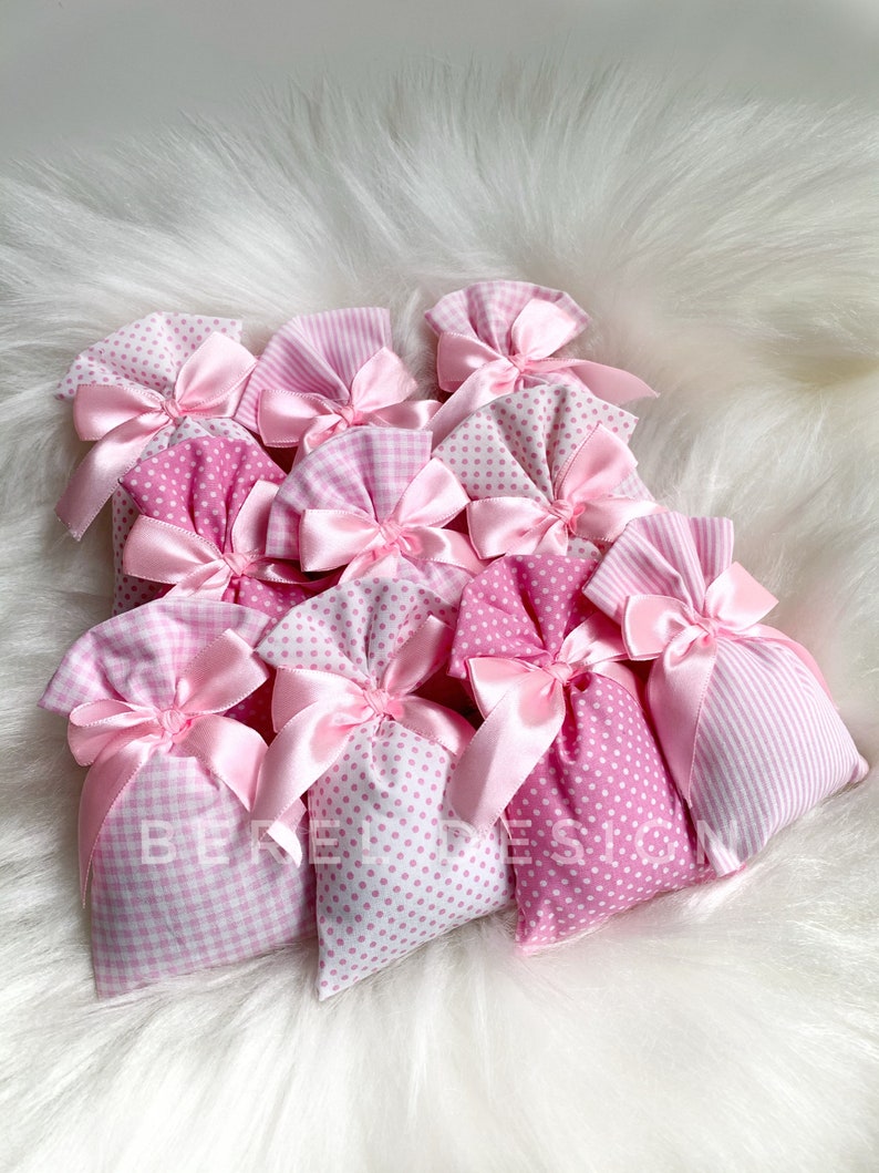 May include: A group of pink fabric gift bags with white polka dots and gingham patterns. The bags are tied with pink satin ribbon bows.