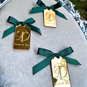 May include: Three gold mirror tags with green ribbon bows. Each tag has the letters "T" and "D" intertwined and the text "Tiandra & Tray" below.