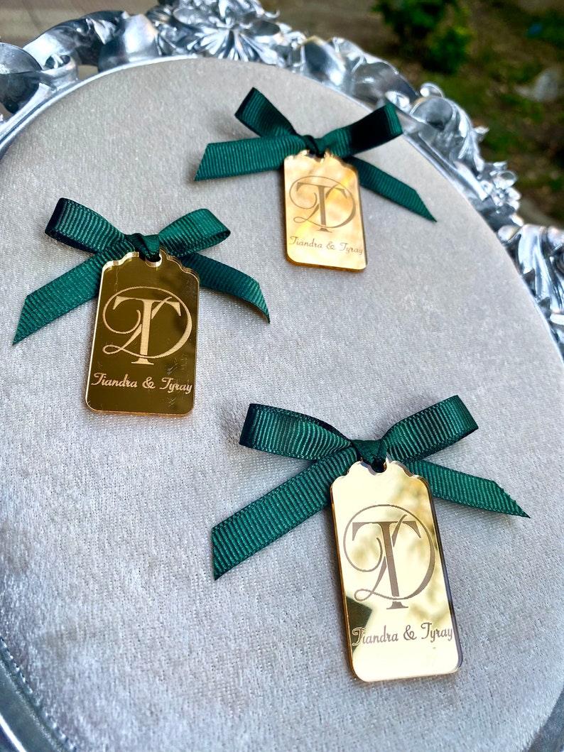 May include: Three gold mirror tags with green ribbon bows. Each tag has the letters "T" and "D" intertwined and the text "Tiandra & Tray" below.