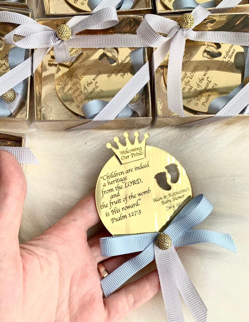 May include: Gold mirror with a crown and the text "Welcoming Our Prince" and "Children are indeed a heritage from the LORD, and the fruit of the womb is His reward." Psalm 127:3.  The mirror is tied with a blue ribbon and a gold button.