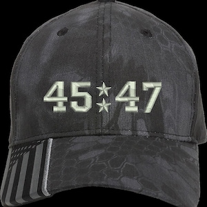 May include: A black camouflage baseball cap with a white embroidered design featuring the numbers "45**47". The bill of the cap has a black and white American flag design.
