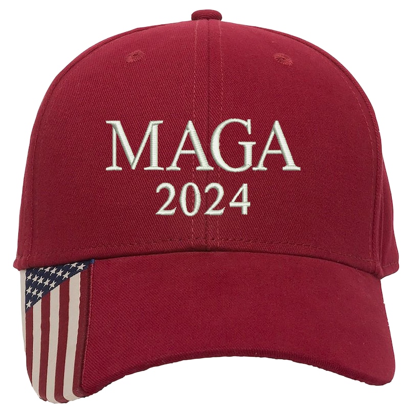 K&ouml;nnte beinhalten: Rote Baseballkappe mit einer wei&szlig;en gestickten amerikanischen Flagge an der Seite und dem Text "MAGA 2024" auf der Vorderseite.