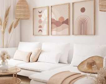 May include: Three abstract art prints with a boho theme. The prints feature a sun, moon, and rainbow with a neutral color palette of beige, brown, and pink. The prints are framed in natural wood and hung on a white wall above a white couch.