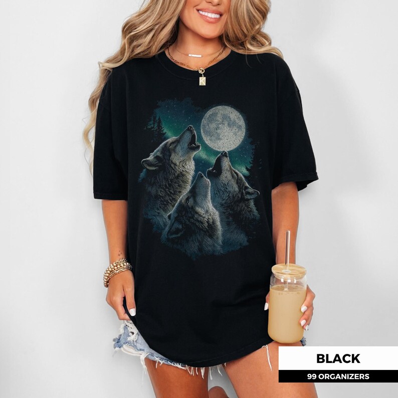 Three howling wolves face the full moon beneath a forest night sky, with textured fur details and a soft teal glow mimicking northern lights. The design blends mystical energy and retro 90s wilderness vibes — perfect for forest lovers and vintage shirt collectors.