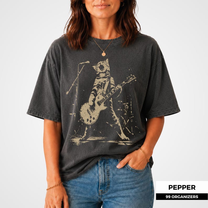 Rock cat artwork featuring a tabby cat in a powerful wide-legged stage pose while playing electric guitar and howling into a microphone. Distressed ink, concert lighting, and background drum equipment give the illustration a vintage band merchandise feel. The design combines feline humor with punk attitude, making it a memorable choice for cat dads, cat moms, musicians, music lovers, and alternative clothing fans.