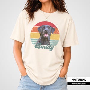 Personalized pet photo tee featuring a custom dog portrait framed by a circular retro sunset with distressed multicolor stripes and a nostalgic vintage finish. The dog’s name appears prominently underneath in cream script lettering. This custom design also works with cat photos, making it a thoughtful personalized gift for pet parents, dog and cat lovers, birthdays, holidays, adoption celebrations, pet memorials, and anyone who wants to wear a portrait of their companion.