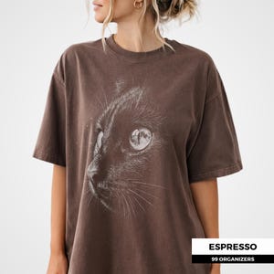 shading and engraved style lines. The cat’s eye reflects a full moon, creating a subtle celestial theme. The high contrast monochrome design gives it a vintage and mysterious aesthetic.