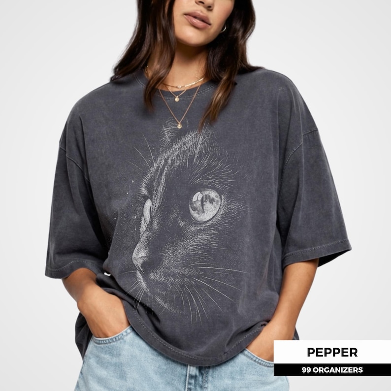 Gothic cat shirt featuring a close up of a black cat’s face with detailed halftone texture and a moon reflection in the eye. The monochrome design creates a dark and atmospheric aesthetic, making it a great graphic tee for cat lovers and fans of mystical art.