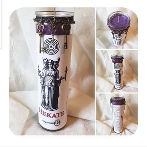 May include: A tall, cylindrical candle with a purple wax top and a decorative metal chain. The candle features a black and white illustration of a goddess and the word "HEKATE". Antique-style keys dangle from the chain.