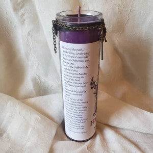 May include: A purple candle in a glass jar with a black chain and ribbon around the top. The candle has a label with text and a drawing of a figure. The text includes the words "Hekate" and "Lovely Lady".