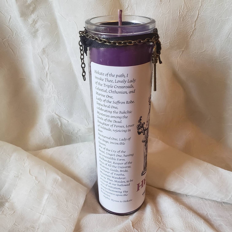 May include: A purple candle in a glass jar with a black chain and ribbon around the top. The candle has a label with text and a drawing of a figure. The text includes the words "Hekate" and "Lovely Lady".